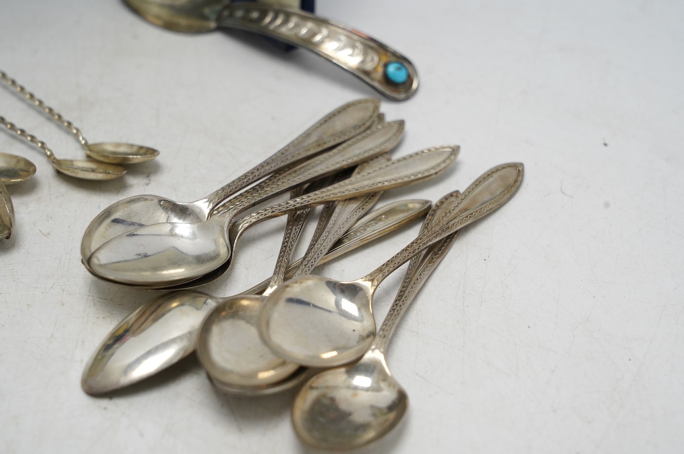 A set of ten George V silver coffee spoons, Birmingham, 1931, a later cased set of six silver and polychrome enamel bean end coffee spoons, a turquoise set sterling spoon, and a set of six white metal spoons with hardsto